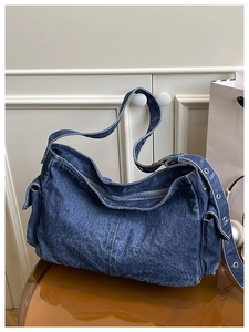 Detail of blue denim hobo bag featuring a side flap pocket and adjustable metal eyelets