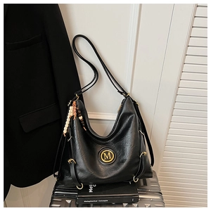 Détail du sac en similicuir noir avec logo M doré, texture plissée et breloque en perles