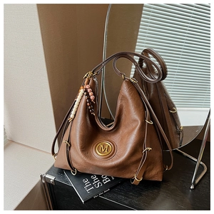 Détail d'un sac cabas en cuir marron avec logo M et charme perlé sur des livres