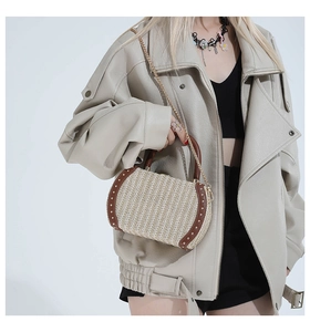 Detail of straw woven crossbody bag with brown leather trim, gold rivets and chain strap