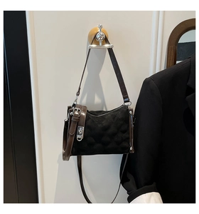 Close-up of quilted black crossbody bag with brown leather straps and metal buckle on wall