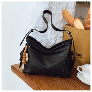 Detail einer Vintage-Schultertasche aus schwarzem Leder mit Perlenquaste auf Holztisch