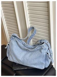 Detail of light blue denim hobo bag with adjustable eyelet strap on leather stool