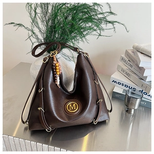 Détail du sac cabas en similicuir marron avec logo M doré et pompon en perles de bois