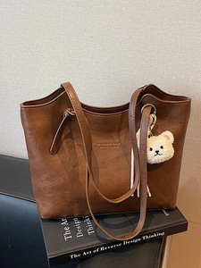 Brown minimalist tote bag with plush bear charm and golden logo on a design book