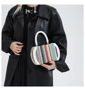 Rainbow woven cylinder bag with white handle and metal rivets shown on a black coat