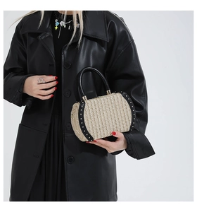 Close-up of woven straw handbag featuring black leather trim and gold rivet details
