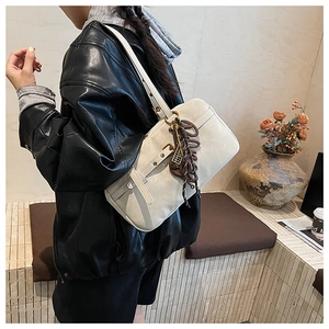 Detail of a chic cream leather underarm bag featuring a unique letter charm and buckle strap