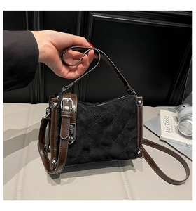 Close-up of black quilted suede handbag with brown leather trim and silver metal buckle