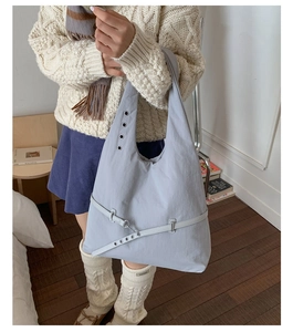 Detail view of grey-blue tote bag with metal eyelets and decorative strap in home setting