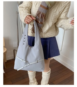 Detail view of large gray tote bag with metallic eyelets and decorative bottom strap