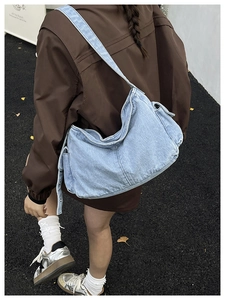Detail of light blue denim crossbody bag featuring contrast stitching and wide strap