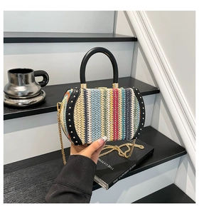 Detail of colorful woven handbag with black leather trim, gold studs, and round handle