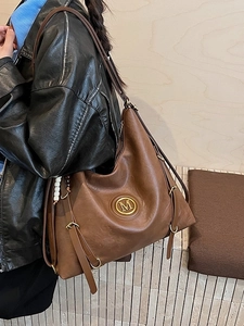 Grand sac cabas vintage en cuir marron foncé avec logo M doré porté par un modèle