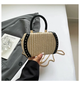 Detail of woven straw handbag with black leather trim, gold studs, and chain strap