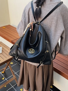 Sac à dos hobo noir polyvalent avec logo M doré et pompon dans un décor d'automne