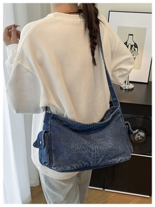 Close-up of a large vintage dark blue denim crossbody bag worn by a model in casual style