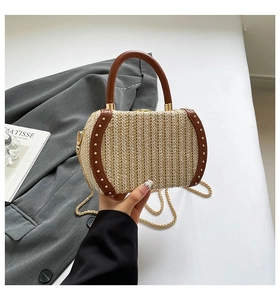 Detail of woven straw handbag with brown leather trim and golden rivets in lifestyle setting