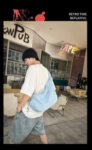 Close-up of light blue nylon crossbody bag with white embroidery on urban street background