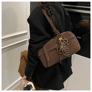 Detail of coffee brown suede shoulder bag with decorative belt buckle and letter charm