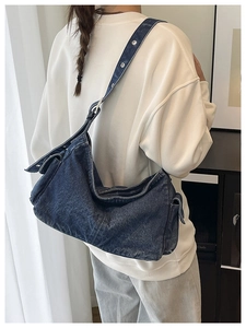 Detail of blue denim crossbody bag with silver eyelets and side pocket styling
