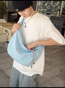 Street style shot of light blue large capacity nylon shoulder bag with white logo