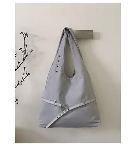 Detail of light grey nylon shoulder bag with silver eyelets and decorative belt