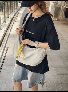 Outdoor street style shot showing the spacious off-white nylon crescent bag with yellow drawstrings