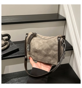 Detail of taupe suede handbag with diamond quilt texture and dark brown wax leather trim