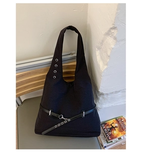 Detail of black canvas shoulder bag featuring metal eyelets and leather strap accents