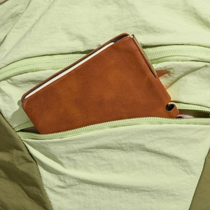 Detail of a brown leather tablet protective sleeve tucked into a green nylon bag pocket