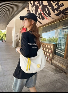 Street style shot of a white crescent crossbody bag with yellow drawstrings and logo
