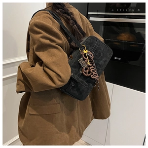 Detail of vintage black shoulder bag with decorative charms worn over a brown blazer