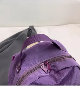 Detail of purple plaid backpack featuring dual zipper closure and reinforced nylon handle