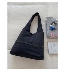 Flat lay of a black nylon tote bag with decorative strap detail on white fabric