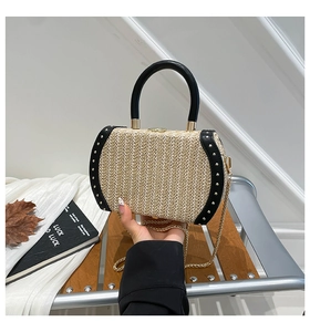 Detail of woven straw bag with black leather trim, golden studs, and metal chain strap