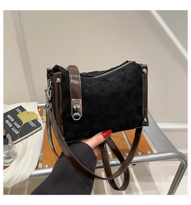 Detail of a black quilted suede handbag with brown leather straps and silver metal hardware