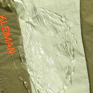 Close-up of waterproof fabric showing water droplets on green nylon outdoor backpack