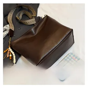 Detail of soft brown leather bucket bag with wide woven strap and beaded charm