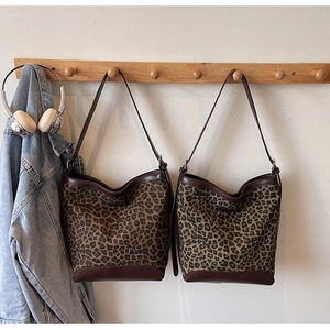 Detail view of large leopard print bucket bags with leather trim hanging on wooden hooks