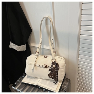 Detail of a creamy white underarm bag with metal rivets on straps and letter charm