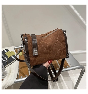 Detail of brown faux suede crossbody bag featuring beige quilted stitching and silver clasp