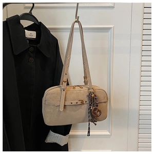 Detail of beige vintage shoulder bag with metal buckle strap and logo charm on black coat