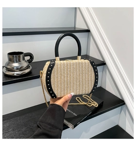 Close-up of woven straw handbag featuring black leather trim and gold metal studs