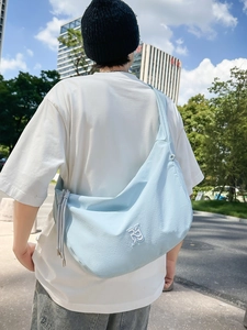 Light blue nylon crescent crossbody bag featuring white logo embroidery and side drawstring