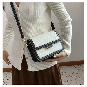 Détail d'un sac carré chic en peluche contrastée avec plaque de marque kavia dorée