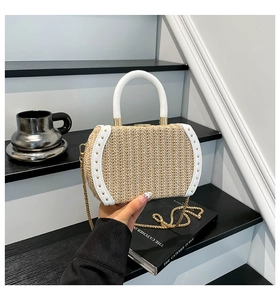 Detail of woven straw bag featuring white leather handles, gold studs and chain strap