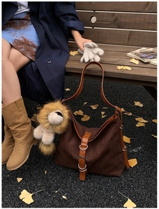 Detail of suede bucket bag with brown leather strap and cute plush lion pendant outdoors