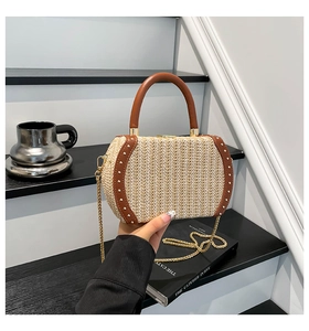Detail of hand-woven straw bag with leather trim, gold rivets and metal chain strap