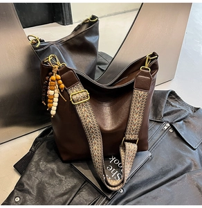 Detail of dark brown leather tote with woven bohemian strap and beaded pendant charm